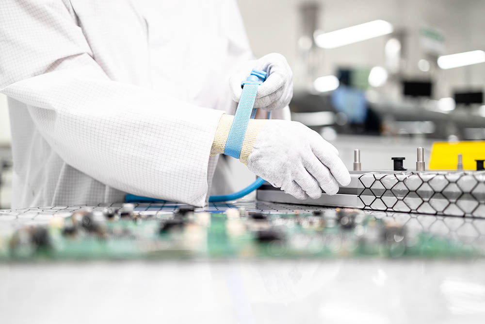 Working in electronics factory. Worker putting on anti static wristband or grounding bracelet while testing electronic components in production.