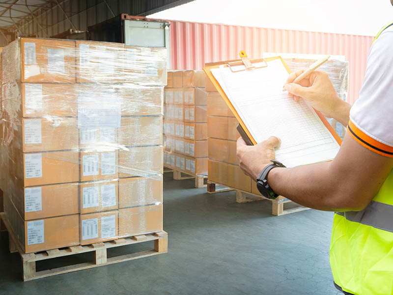Worker holding clipboard inspecting checklist of packaging boxes