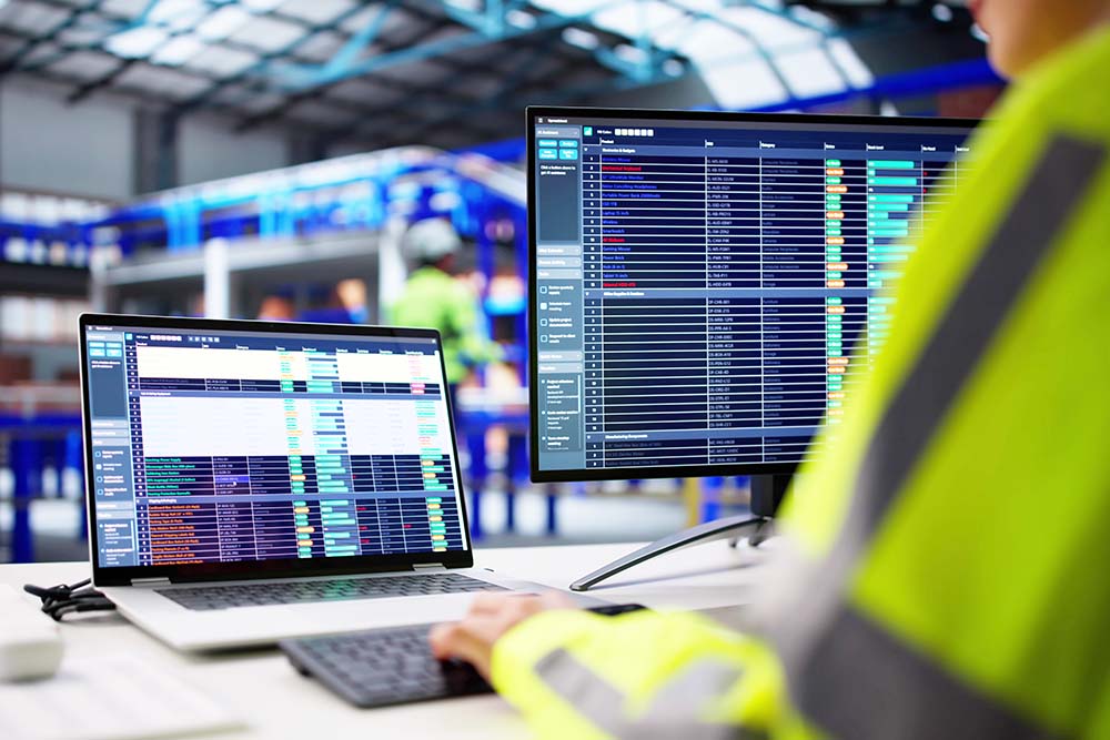 Warehouse Worker Uses Logistic Software To Manage Inventory And Orders. Woman In Business Office Monitors Spreadsheets