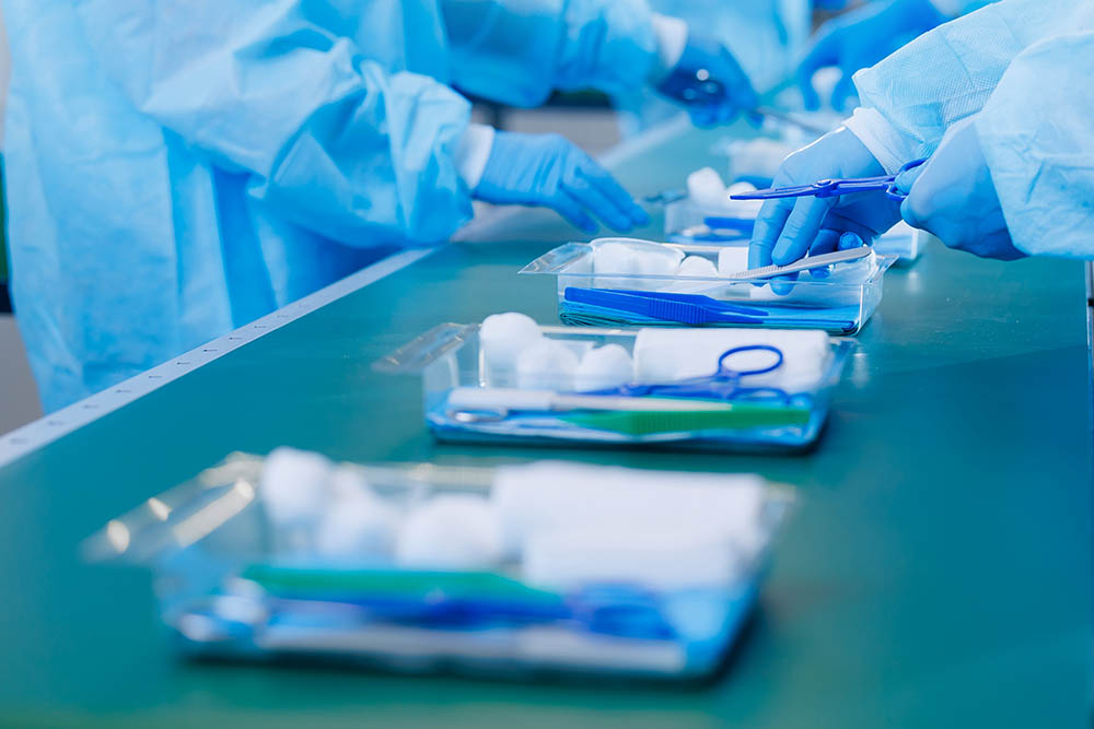 medicine factory, sterile box production line for medical instruments and surgical kits. workers in uniformed pack scalpels, clamps, tweezers and bandages on conveyor belt