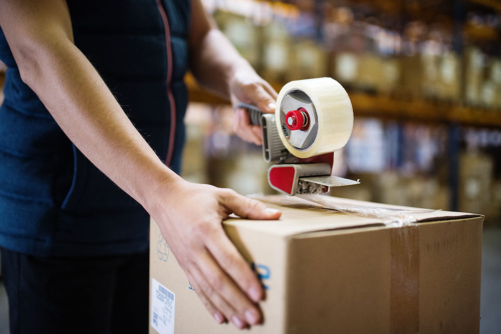 male warehouse worker sealing cardboard boxes.